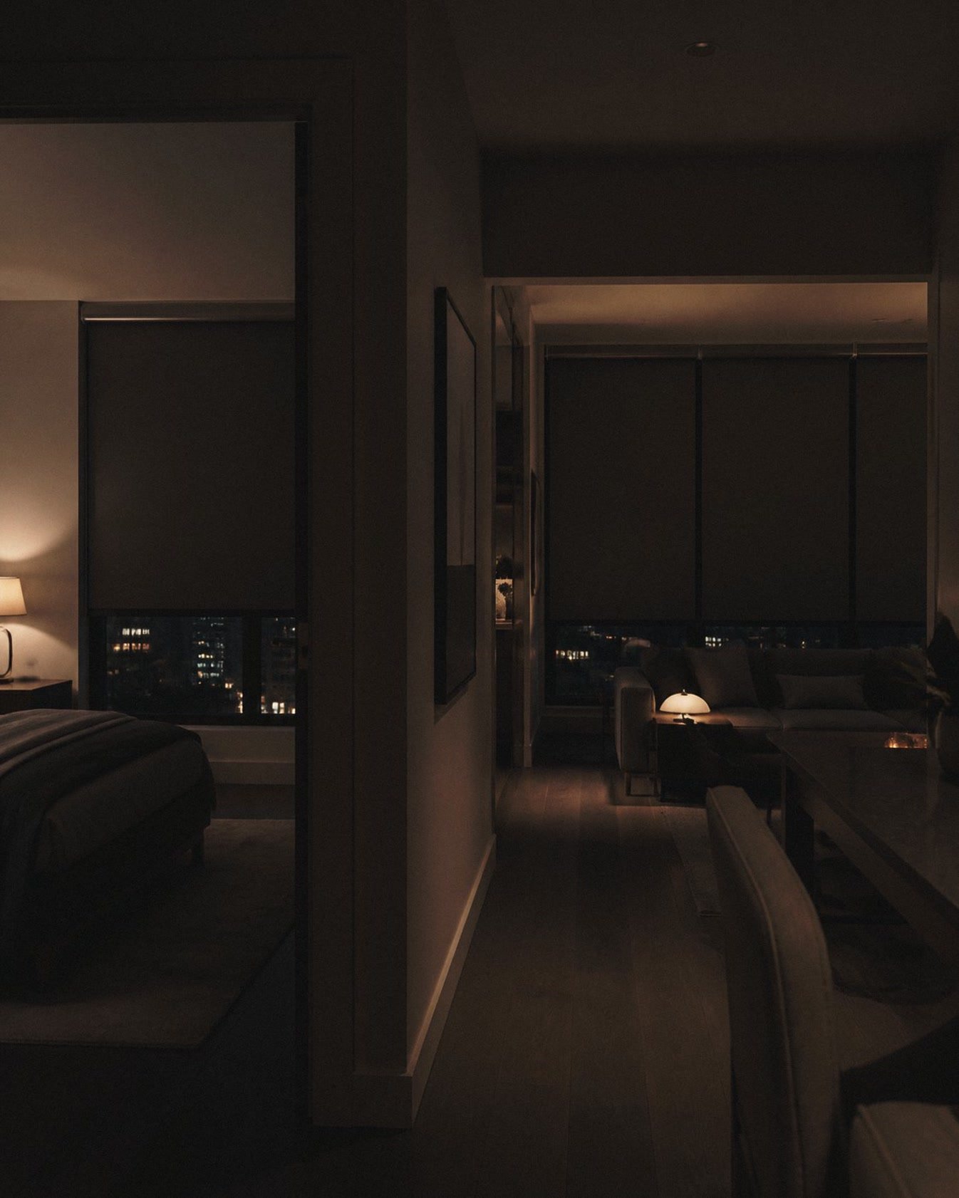 Une chambre sombre le soir, occultant descendu et la ville dehors.